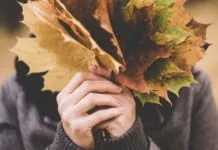 Vrouw verbergt haar gezicht achter herfstbladeren
